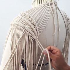 a person is holding something in front of a mannequin's head with white yarn on it