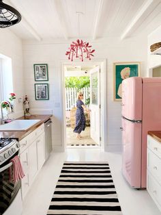 a pink refrigerator in a white kitchen with black and white striped rug on the floor