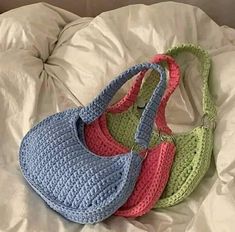 three crocheted purses sitting on top of a white bed covered in sheets