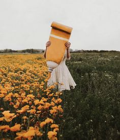 a woman in white dress holding up a yellow box over her head while standing in a field of flowers