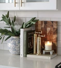 a candle and some books on a white counter top next to a potted plant