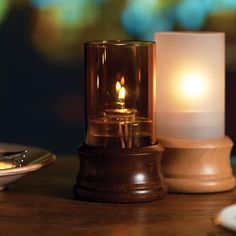 a lit candle sitting on top of a wooden table next to a plate and spoon