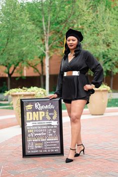 a woman standing next to a sign on a brick walkway with trees in the background