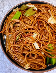 a bowl filled with noodles and vegetables on top of a marble countertop next to a fork