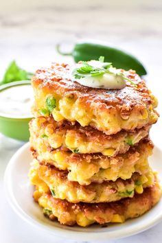 a stack of crab cakes on a white plate next to a bowl of ranch dressing