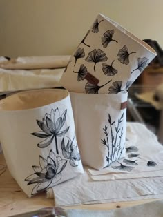 two vases sitting on top of a table covered in white paper and black flowers