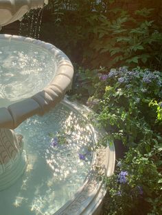 a water fountain in the middle of a garden with flowers and plants around it,