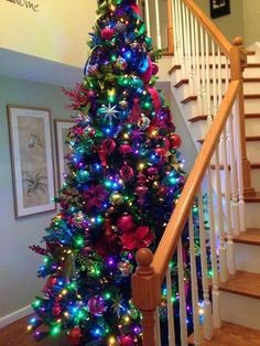 a brightly colored christmas tree in the corner of a room next to a stair case