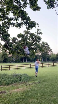 two people are flying through the air on a swing set in a grassy field near a fence