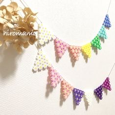 some colorful beads hanging from a string on a white surface with flowers in the background