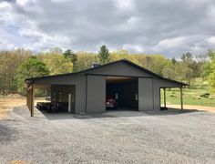 a large garage with a car in it on gravel lot next to trees and grass