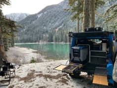 an off road vehicle parked next to a lake in the woods with mountains in the background