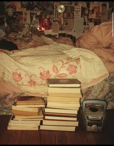 a pile of books sitting on top of a bed next to an alarm clock and cell phone