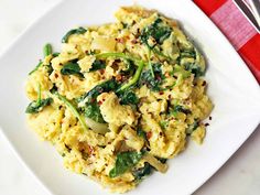 spinach scrambled eggs on a white plate with fork and red checkered table cloth