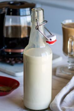 a glass bottle filled with milk sitting on top of a table next to a cup