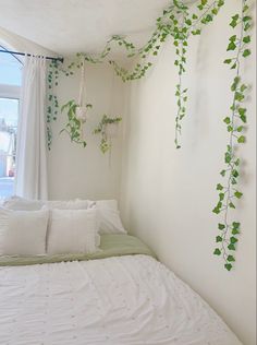 a bed with white linens and green plants on the wall above it, in front of a window