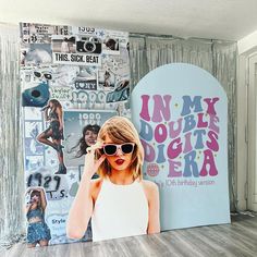 a woman wearing sunglasses standing in front of a wall with pictures on it and an advertisement behind her