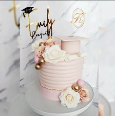 a pink and gold graduation cake with flowers on the top is displayed in front of a white marble background