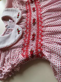 This beautiful red dotted baby girl dress hand smocked in red and hand embroidered with beautiful red flowers . The dress completes it's look with white Peter Pan collar and beautiful smocked puffed sleeves. Dress is fully lined with a soft cotton material. The back closes with a zip and tie sashes. 3-6 months & 6-12 months sizes come with a bow attached headband. Size 1 onwards come with a bow clip. Material Outside- 100% Cotton Lined with soft cotton fabric Recommend Dry clean only Available s Sweet Red Short Sleeve Dress, Fitted Red Cotton Smocked Dress, Red Cotton Dress With Smocked Bodice, Red Fitted Cotton Smocked Dress, Red Cotton Dress With Smocked Back, Red Cotton Smocked Dress With Smocked Bodice, Red Smocked Dress With Ruffles And Short Sleeves, Fitted Red Smock Dress, Cute Red Smock Dress