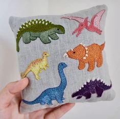 a hand holding a pillow with different colored dinosaurs on it