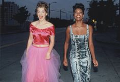 two women in dresses walking down the street at night, one wearing a pink and blue dress