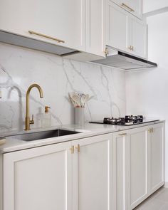 a kitchen with white cabinets and marble counter tops, gold faucets and brass handles