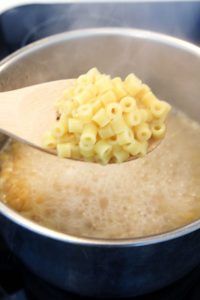 a wooden spoon full of macaroni and cheese being stirred in a saucepan