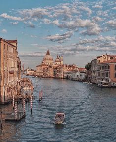 a boat traveling down a river next to tall buildings and clouds in the sky above