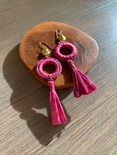 two pink tasselled earrings sitting on top of a wooden plate next to each other