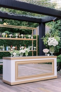 an outdoor bar is decorated with white flowers and greenery, along with shelves filled with liquor bottles