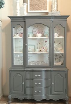 the china cabinet is painted gray with white trimmings and has glass doors on it