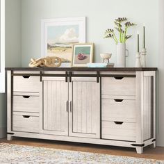 a sideboard with drawers and pictures on top of it in a room next to a window