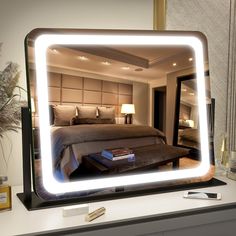 a large lighted mirror on top of a desk next to a lamp and a bed