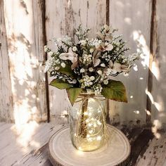 a vase filled with white flowers sitting on top of a wooden table next to a wall