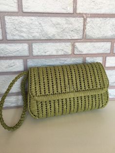 a green woven purse sitting on top of a table next to a white brick wall