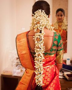 the back of a woman's head with white flowers in her hair and an orange saree