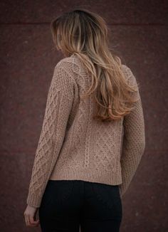 a woman with long hair wearing a sweater and black pants standing in front of a brick wall