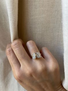 a woman's hand wearing a gold ring with two diamonds on it, against a beige background