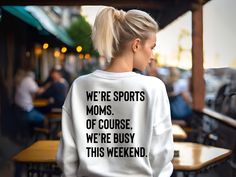 a woman wearing a sweatshirt that reads we're sports moms of course, we're busy this weekend