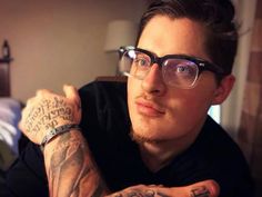 a man with tattoos on his arms and arm is looking at the camera while wearing glasses