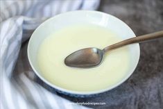 a white bowl filled with milk and a spoon on top of the bowl is sitting on a gray table cloth