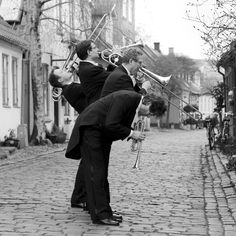 three men in suits playing musical instruments on a cobblestone street