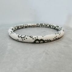 a white and black snake skin bracelet with silver clasps on a gray surface,