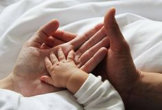 a person holding a baby's hand while laying on top of a white blanket