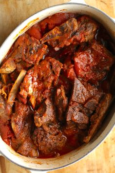 a pot filled with meat and sauce on top of a wooden table