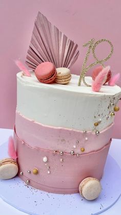 a pink and white cake decorated with macaroons, seashells and a fan