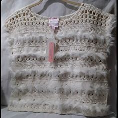 a crocheted sweater with white feathers hanging on a clothes hanger in front of a bed