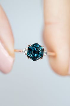 a woman's hand holding an engagement ring with a blue diamond