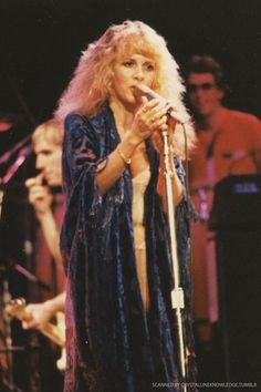 a woman with blonde hair holding a microphone in front of other people and singing on stage