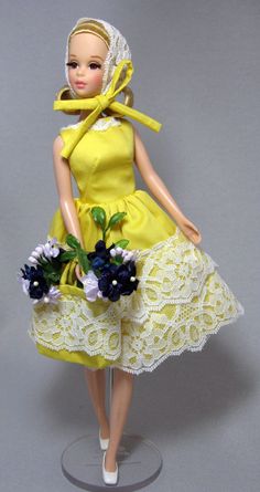 a doll wearing a yellow dress with white lace on the skirt and flowers in her hand